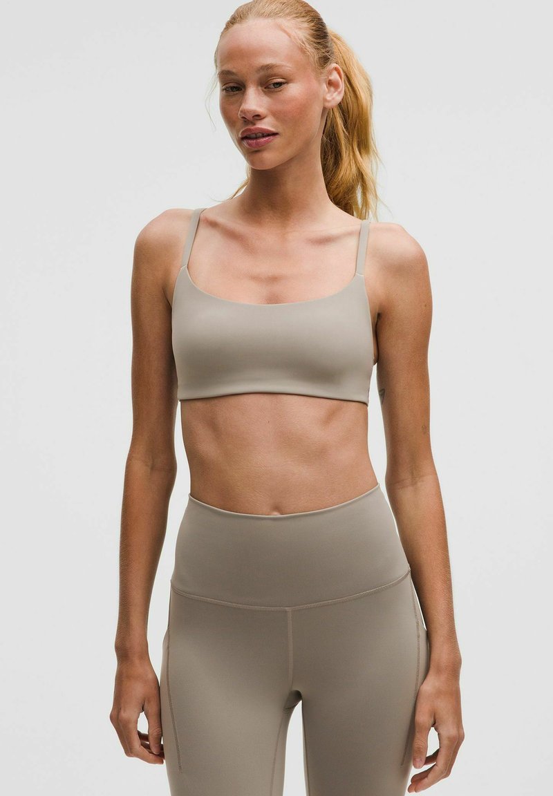 Bralette atlético beige con tirantes finos, textura suave y escote cuadrado, combinado con leggings beige de cintura alta.
