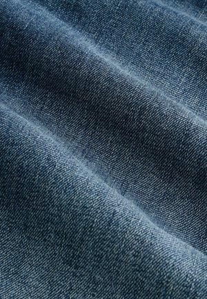 Tessuto di denim in blu medio, caratterizzato da una trama sottile con intrecci diagonali e un drappeggio morbido, che mostra variazioni naturali di colore.