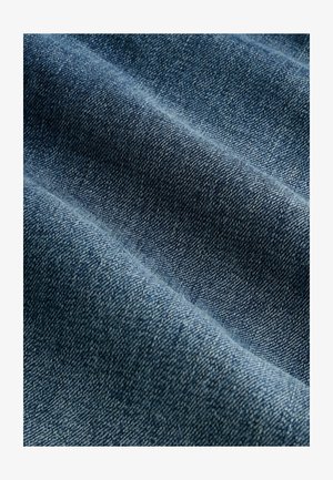 Tessuto di denim in blu medio, caratterizzato da una trama sottile con intrecci diagonali e un drappeggio morbido, che mostra variazioni naturali di colore.