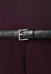 Cinturón de cuero negro con hebilla rectangular plateada, presenta una superficie texturizada y varios agujeros, usado sobre una tela de color burdeos oscuro.