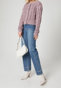 Ljuslila kabelstickad tröja, högmidjade blå jeans, vit handväska och blanka beige blockklackade stövlar. Enkel, modern design.