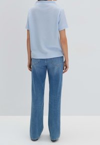 Polo shirt azzurro chiaro, testurizzato e con maniche corte, abbinato a jeans azzurro chiaro a gamba ampia con tasche posteriori.