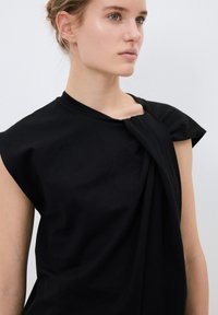 T-shirt nera con vestibilità ampia, caratterizzata da un design annodato sulla spalla e maniche corte a campana. Realizzata in morbido cotone.