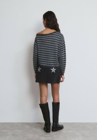 Suéter grande a rayas grises y negras con diseño de un solo hombro, combinado con una falda negra de mezclilla que presenta dos detalles de estrellas plateadas.