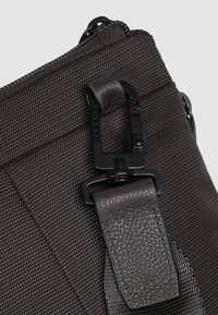 Dunkelbraune, strukturierte Stofftasche mit matter Oberfläche, ausgestattet mit einem schwarzen Metallverschluss und Lederdetails am Tragegurt, die ein modernes Design unterstreichen.