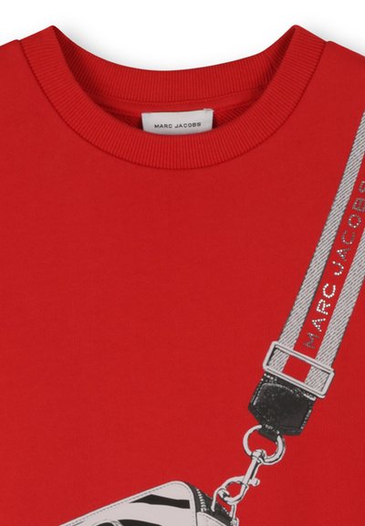 Sweat-shirt rouge avec un col rond côtelé et une illustration d'un sac avec une sangle grise, ornée du texte "MARC JACOBS".