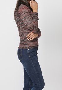 Haut à manches longues en maille rouge, noir et gris avec un motif texturé. Accordé avec un jean en denim bleu comportant une poche arrière décorative.