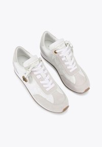 Sneakers bianchi e grigio chiaro realizzati in pelle e camoscio, con lacci bianchi piatti, dettagli in oro e un pannello laterale testurizzato.