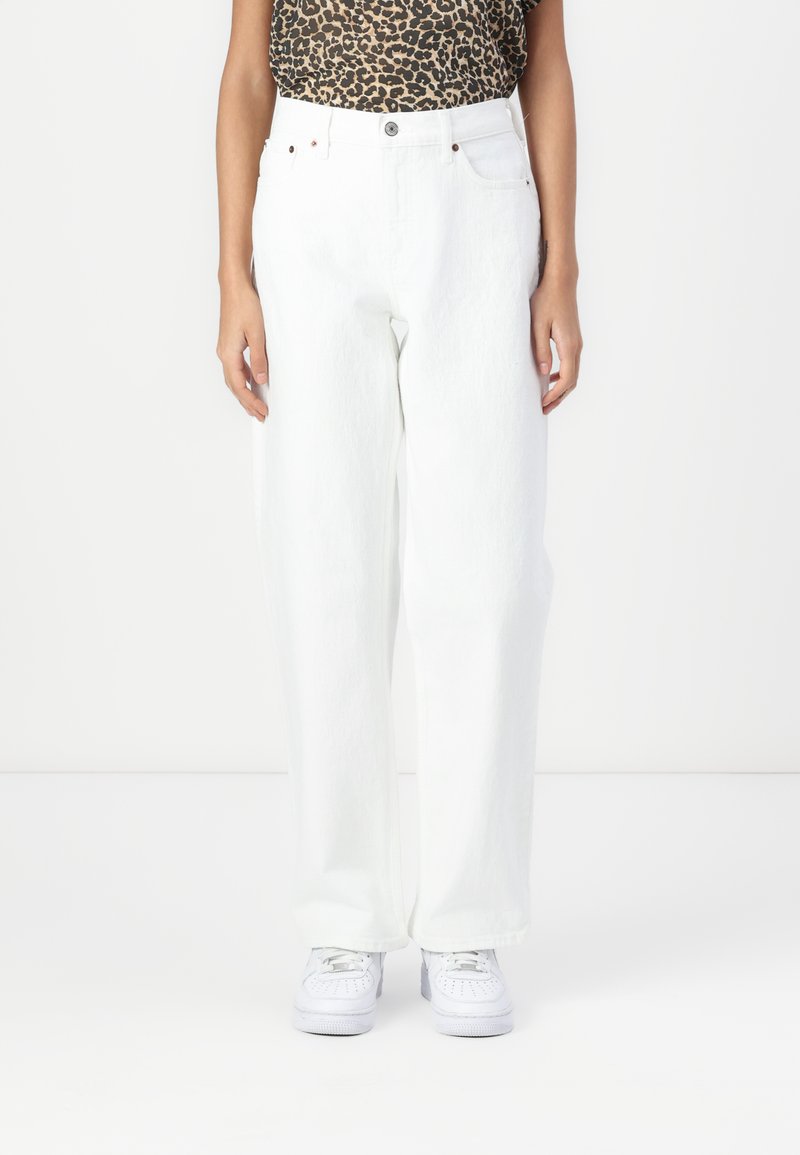 Vita vida jeans med hög midja, tillverkade av denim, med fem fickor och metalldetaljer. Bärs med vita sneakers.