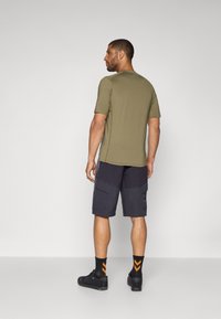 Chemise olive à manches courtes associée à un short cargo bleu marine. Des baskets noires et des chaussettes orange à motifs complètent la tenue.