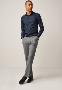 Marineblå skjorte med knapper og grå stribede bukser, kombineret med sorte sko. Skjorten har en krave, og bukserne har en skræddersyet pasform.