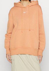 Nike hoodie i mjuk persikofärg med en vit logotyp, dragsko i huvan, framficka och ribbade manschetter och nederkant. Material i bomullsblandning.