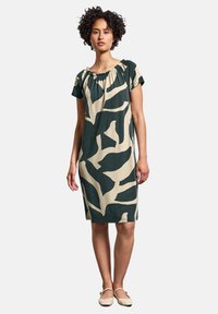 Knälång klänning i grön och beige, med lös passform, korta ärmar och samlad halsringning med abstrakta mönster.