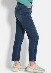 Jean en denim bleu foncé à coupe droite, avec poches arrière et taille mi-haute, accompagnés de baskets de sport de couleur claire.