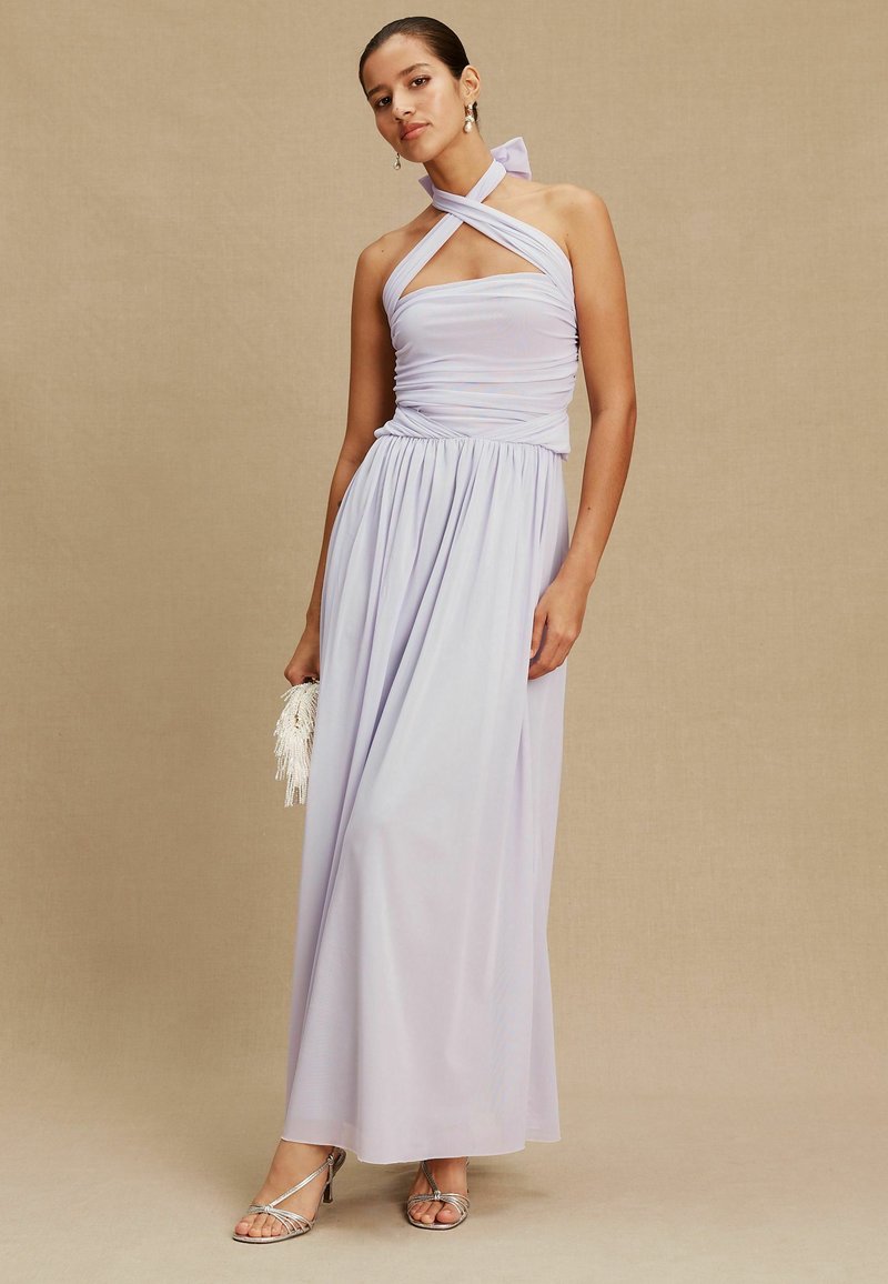 Hellviolettes Neckholderkleid mit figurbetontem Oberteil, geraffter Taille und fließendem Rock. Verziert mit einer Schleife am Hals und silbernen Stilettos.