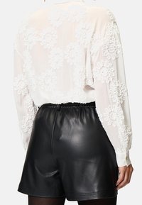 Blouse blanche avec un design floral texturé sur les manches, associée à un short en cuir noir avec une taille élastique. Fini en tissu lisse.