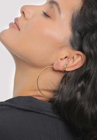 Grand anneau d'oreille doré avec une finition lisse, attaché au lobe de l'oreille, avec un design minimaliste et une surface polie.