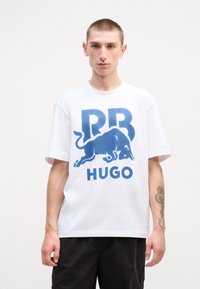 Hvid bomulds T-shirt med et blåt grafisk print med "RR" og et okse-design over "HUGO." Afslappet pasform med korte ærmer.