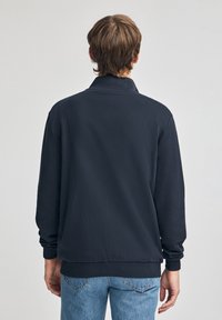 Pullover blu navy a maniche lunghe con scollatura a colletto, realizzato in tessuto morbido. Polsini e orlo a coste, design minimalista, senza loghi o motivi visibili.