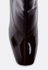 Stivaletto alla caviglia in pelle nera con finitura lucida, punta appuntita e cuciture visibili lungo le cuciture. Design strutturato ed elegante.