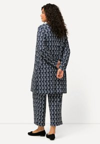 Navyblaue Tunika- und Hosenkombination mit weißen kreisförmigen Mustern, die eine lockere Passform, lange Ärmel und flache schwarze Schuhe aufweist.