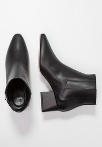 Czarne skórzane botki za kostkę z ostrym noskiem, szerokim obcasem i suwakiem z boku. Gładka tekstura i minimalne detale podkreślają elegancki design.