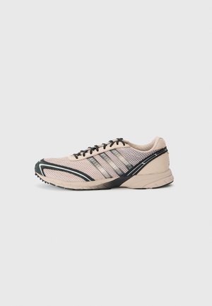 Scarpe da ginnastica leggero in rete beige con accessori neri. Le caratteristiche includono una suola testurizzata, un tallone di supporto e un design a strisce diagonali.