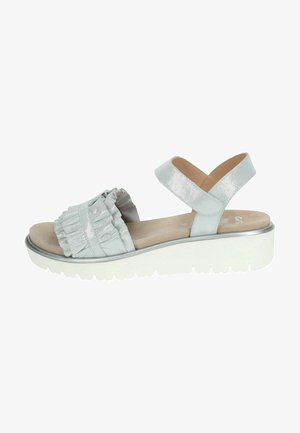 Stříbrné sandály s volánkovým designem a překříženými popruhy, silnou bílou podrážkou a texturovanou tkaninou. Mají otevřenou špičku a polstrovanou stélku.