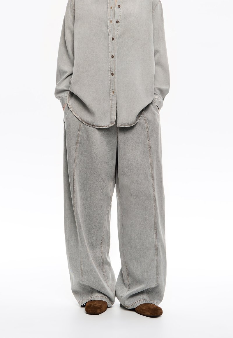 Gray denim shirt with a button placket paired with wide-leg gray denim pants. Soft texture, large pockets, and subtle contrast stitching.