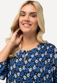 Tummansininen paita, jossa on avainaukko-kaula-aukko, pleatattu pinta ja vaaleansininen sekä valkoinen kukkakuosi, jossa on pisaroita.