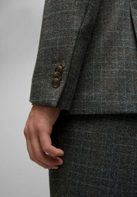 Grau kariertes Tweed-Blazer mit einem plaidmuster, ausgestattet mit einem Vierknopfmanschette und einer ergänzenden Textur am unteren Kleidungsstück.