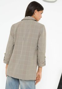 Beige károvaný blazer s vykrojeným límcem, tříčtvrtečními rukávy a zlatými knoflíkovými detaily, s hladkou tkanou strukturou.