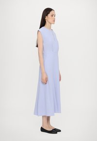 Rochie fără mâneci de lavandă deschisă, cu decolteu în formă de cheie, fustă A-line fluidă și textură de țesătură netedă. Purtați cu ballerini negri.