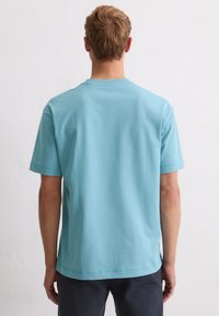 Jasnoniebieska bawełniana koszulka z krótkimi rękawami, okrągłym dekoltem i prostym krojem. Gładka faktura z minimalnymi detalami szwów przy dolnej krawędzi i rękawach.