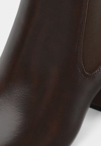 Brūni ādas potītes zābaki ar gludu tekstūru, elastīgām sānu daļām un noapaļotu pirkstu ar zemu paugurknābju papēdi.