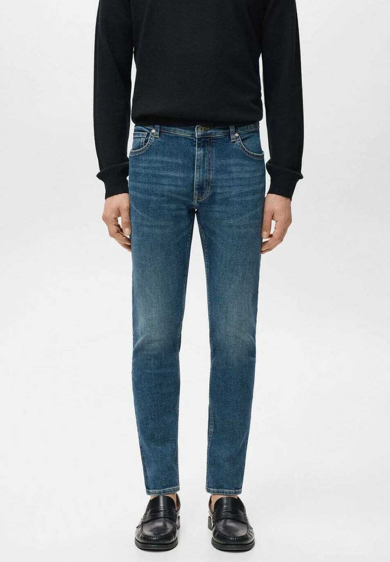 Tumma siniset kapeat farkut, joissa on etutaskut, kevyet kulutusjäljet ja kapea istuvuus, yhdistettynä mustiin kiiltäviin juhlakengiin.