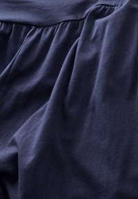 Marineblåt stof med en glat tekstur, der har sammenrullede detaljer langs den øverste søm, hvilket skaber en afslappet drapering og blød fremtoning.