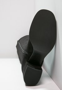 Czarne zamszowe botki o eleganckim designie, z gładkim, zaokrąglonym noskiem i płaską, teksturowaną czarną podeszwą. Widoczny detal zamka bocznego.