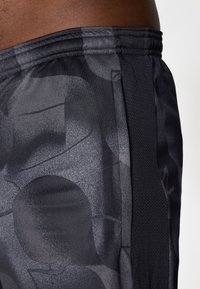 Sorte atletiske shorts med et teksturert, abstrakt mønster. Bena har mesh-detaljer og elastisk midjebånd for komfort og fleksibilitet.
