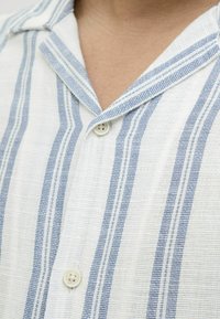 Chemise rayée avec des lignes bleues et blanches, en tissu léger, design à col, avec une fermeture par boutons à l'avant et une surface texturée.