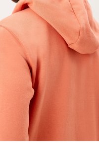 Weicher Kapuzenpullover mit lockerem Schnitt, ausgestattet mit einer Kordelzugkapuze, glatter Textur und sichtbaren Nahtdetails entlang der Nähte.