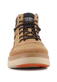 Baskets montantes en suede et cuir beige avec des accents noirs, des lacets orange et une semelle en caoutchouc texturée. Présente le logo sur la languette et sur le côté.