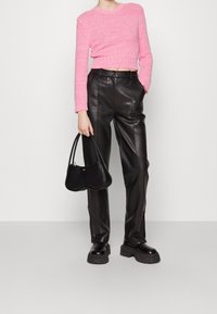 Háčkovaný růžový svetr, krátký design, struktura s rib kužely. Černé kožené kalhoty s vysokým pasem s hladkým povrchem. Černá kabelka s zakřiveným tvarem.