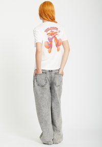 White cotton t-shirt featuring a colorful graphic of a character playing guitar on the back, paired with high-waisted, grey denim jeans.