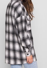 Svart och vit rutigt flanellskjorta med långa ärmar, bröstfickor och knäppning vid ärmsluten. Lös passform och mjuk textur. Bärs med ljusblå jeans.