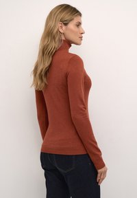 Rostfarbenes Rollkragensweatshirt, taillierte Passform, lange Ärmel, gerippte Bündchen und Saum, weiche Textur, getragen mit dunklen Denim-Jeans.
