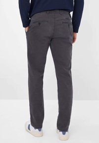 Grå bukser med en glat tekstur, tapered fit og to baglommer. Sammen med hvide og blå sneakers.