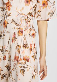Robe florale avec un fond crème ornée de fleurs orange et violettes, une ceinture à la taille et des manches légères en voile. Texture de tissu lisse et léger.