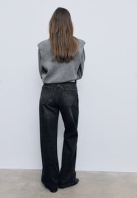 Sivi, oversized pulover s detaljima na ramenima u kombinaciji s visokim, širokim crnim trapericama. Glatka tkanina i minimalno šivanje.