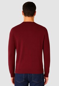 Maglione lavorato a maglia color bordeaux con scollatura a girocollo, maniche lunghe e polsini e orlo a coste, caratterizzato da una texture liscia e un design aderente.